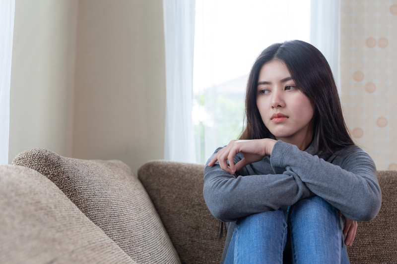 jovem mulher asiática sentada no sofá com aparência triste